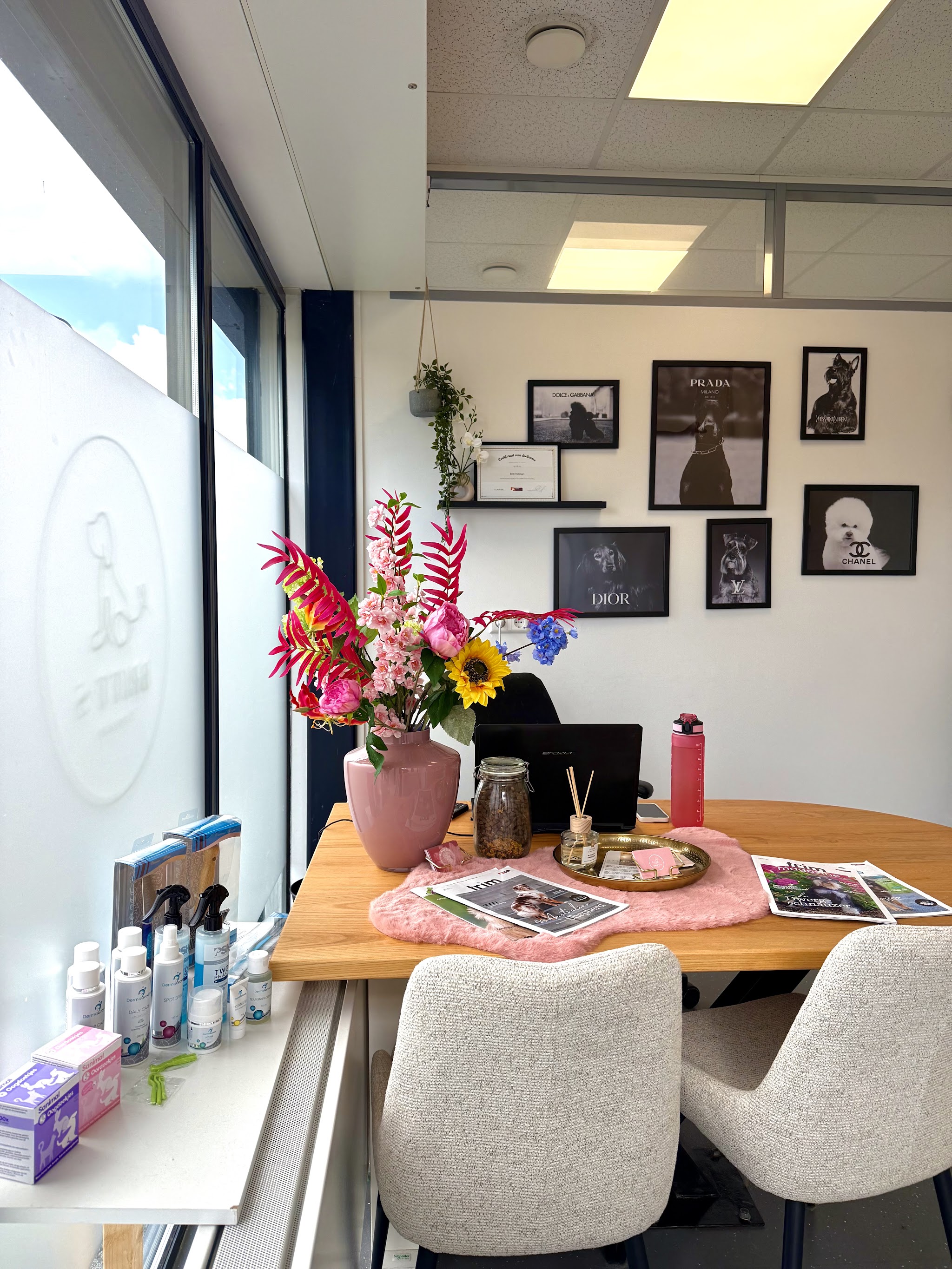 De salon: houten tafel met bloemen, ingelijste hondenprints aan de muur en het logo op het raam